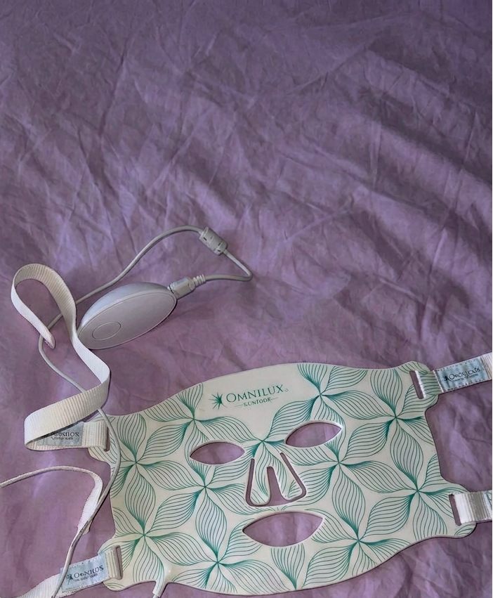 Omnilux LED Face Mask on purple sheets of a bed